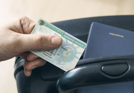 Man holding permanent resident (green) card. United States passport on suitcase. Application to register permanent residence.